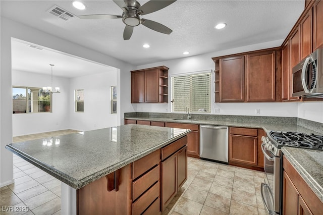 kitchen with appliances with stainless steel finishes, light tile patterned floors, sink, a kitchen island, and decorative light fixtures