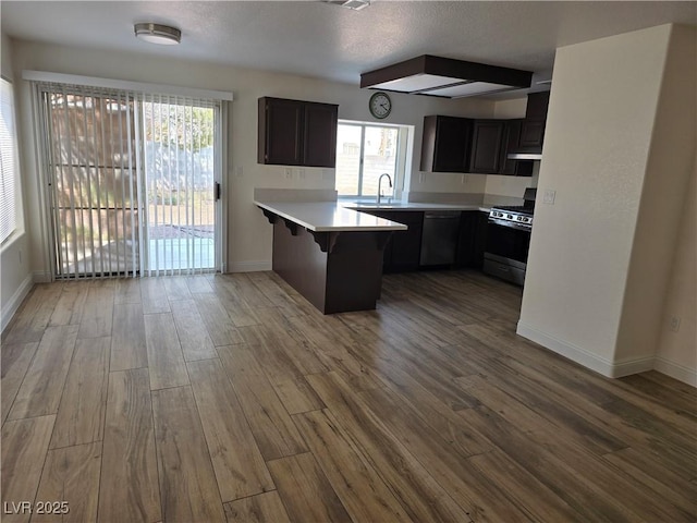 kitchen with appliances with stainless steel finishes, a kitchen breakfast bar, kitchen peninsula, a wealth of natural light, and light hardwood / wood-style floors