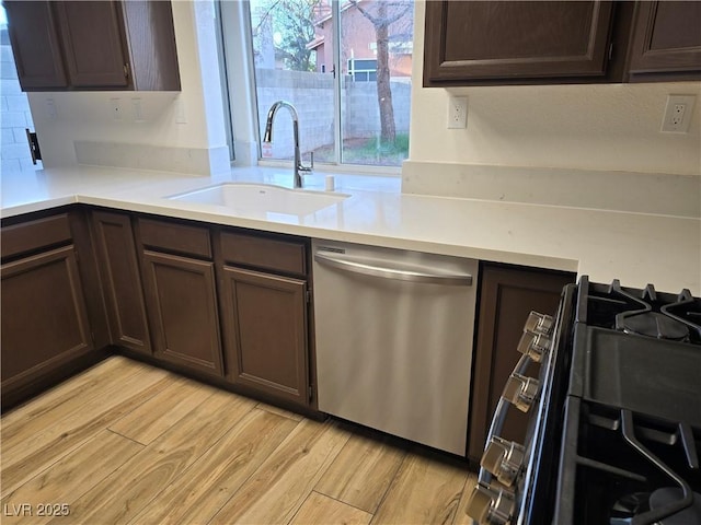 kitchen featuring sink, range with gas cooktop, dark brown cabinets, light wood-type flooring, and stainless steel dishwasher