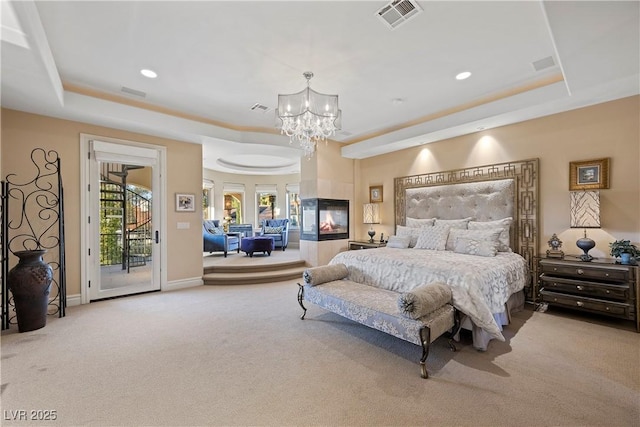 carpeted bedroom with an inviting chandelier, a tray ceiling, access to outside, and a multi sided fireplace