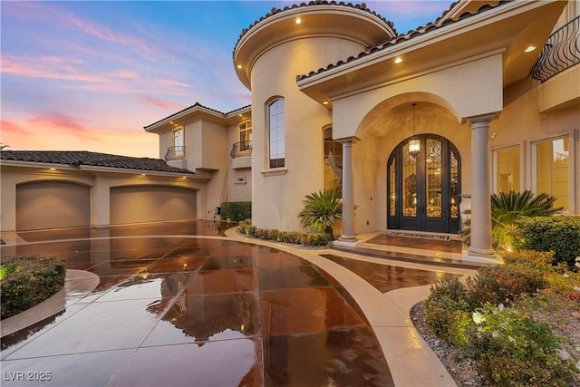 exterior entry at dusk featuring a garage and french doors