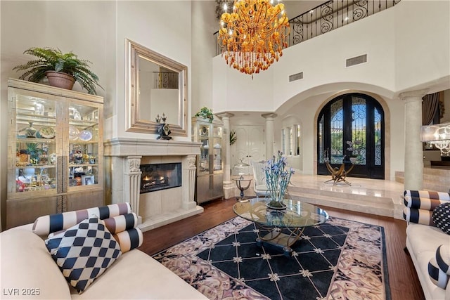 living room with ornate columns, a towering ceiling, a fireplace, a chandelier, and hardwood / wood-style flooring