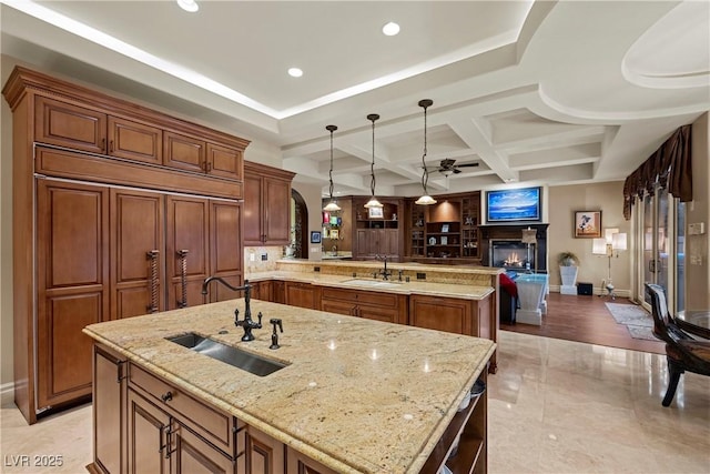 kitchen with sink, hanging light fixtures, coffered ceiling, light stone countertops, and a large island with sink