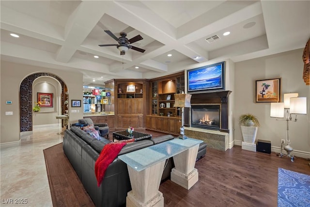 living room with built in shelves, coffered ceiling, dark hardwood / wood-style flooring, ceiling fan, and beam ceiling