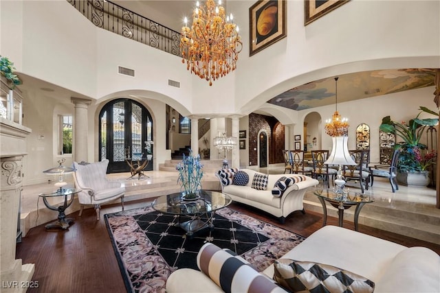 living room featuring ornate columns, dark hardwood / wood-style flooring, a high ceiling, and an inviting chandelier