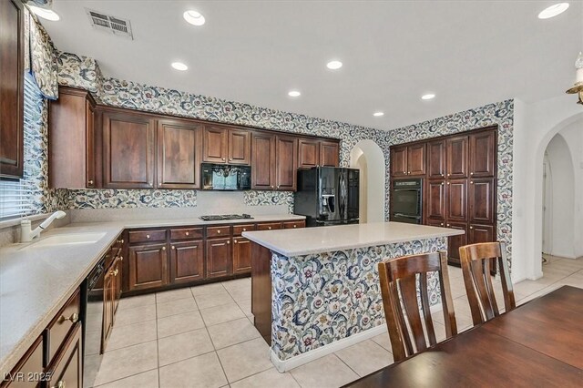 kitchen featuring sink, black appliances, a center island, light tile patterned floors, and backsplash