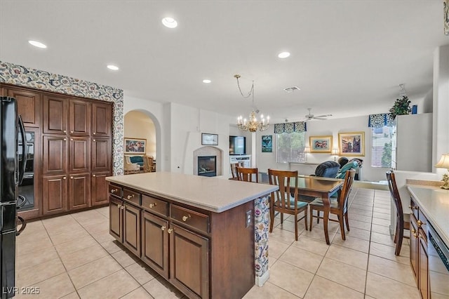 kitchen with light tile patterned floors, black refrigerator, a kitchen island, decorative light fixtures, and stainless steel dishwasher