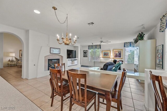 dining room featuring a tile fireplace, ceiling fan with notable chandelier, and light tile patterned floors