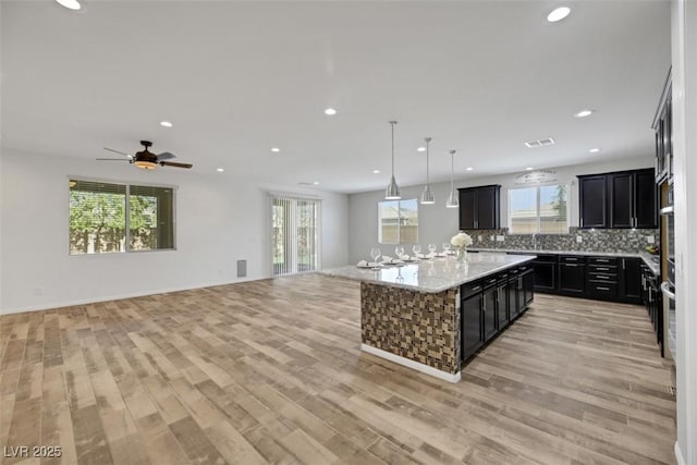 kitchen with light hardwood / wood-style flooring, backsplash, hanging light fixtures, a center island, and light stone counters