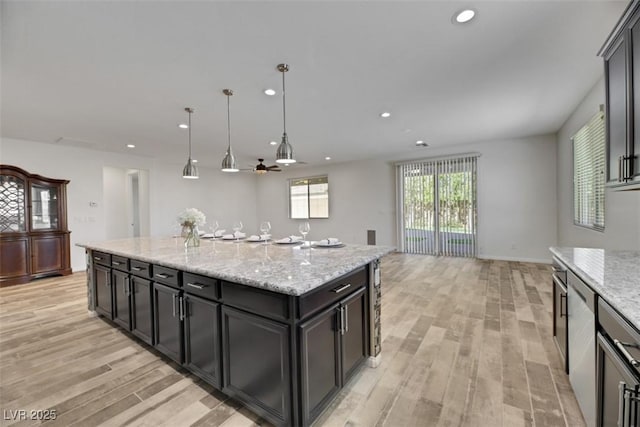 kitchen featuring decorative light fixtures, light hardwood / wood-style flooring, light stone countertops, and a kitchen island