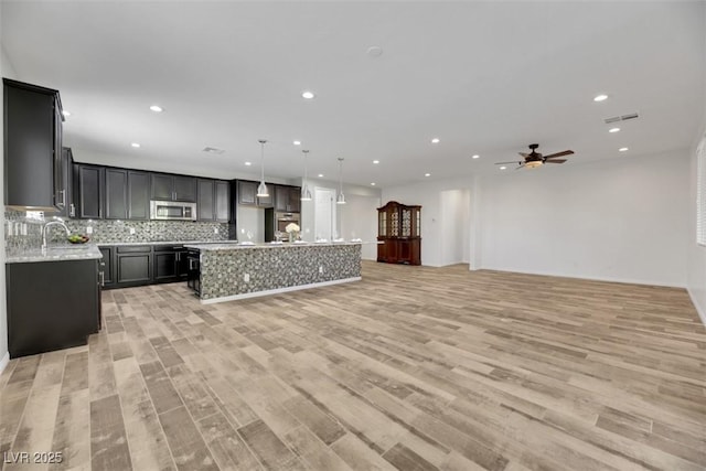 kitchen featuring sink, light hardwood / wood-style flooring, hanging light fixtures, a kitchen island, and decorative backsplash