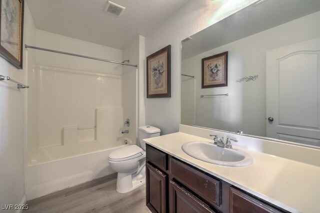 full bathroom with toilet, wood-type flooring, a textured ceiling, shower / bathtub combination, and vanity