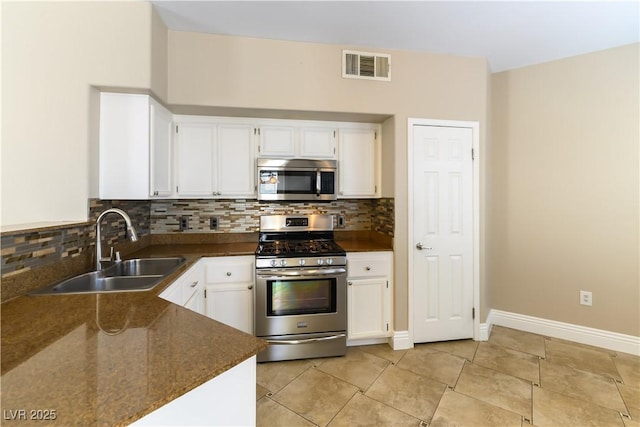 kitchen featuring appliances with stainless steel finishes, sink, white cabinets, backsplash, and dark stone counters