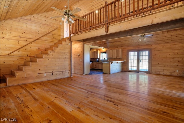 unfurnished living room with wooden walls, wooden ceiling, ceiling fan, and light wood-type flooring