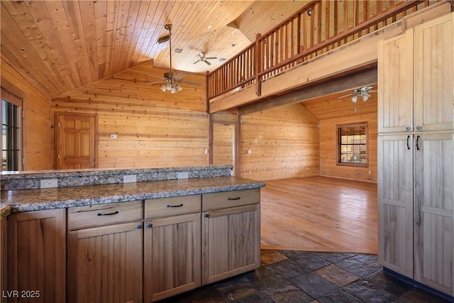 kitchen with lofted ceiling, wood ceiling, ceiling fan, dark stone counters, and wood walls