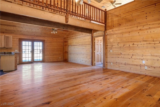 unfurnished living room featuring french doors, wood walls, ceiling fan, and light hardwood / wood-style flooring