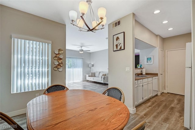 dining area featuring sink, ceiling fan with notable chandelier, and light hardwood / wood-style floors