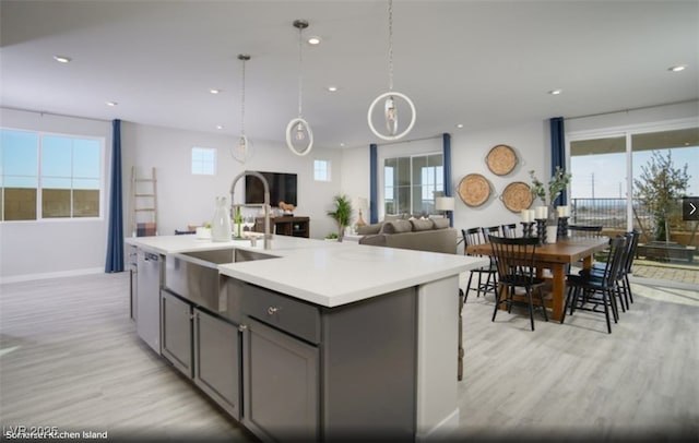 kitchen featuring gray cabinetry, light hardwood / wood-style flooring, stainless steel dishwasher, and an island with sink