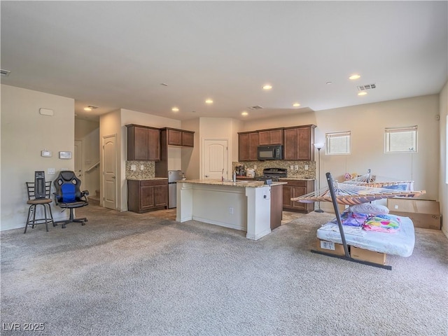 kitchen with a kitchen breakfast bar, decorative backsplash, a kitchen island with sink, light stone countertops, and light carpet