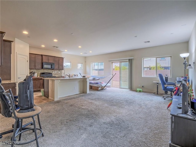 kitchen featuring light carpet, a kitchen breakfast bar, an island with sink, decorative backsplash, and stove