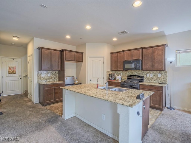 kitchen with light carpet, backsplash, black appliances, and a center island with sink