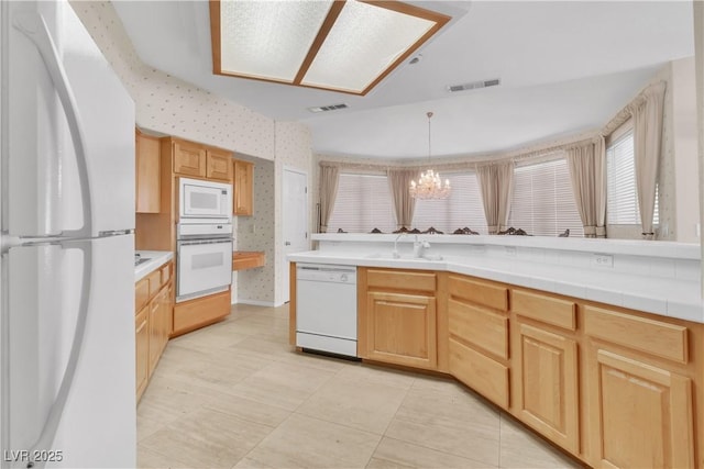 kitchen featuring an inviting chandelier, light brown cabinetry, white appliances, and decorative light fixtures