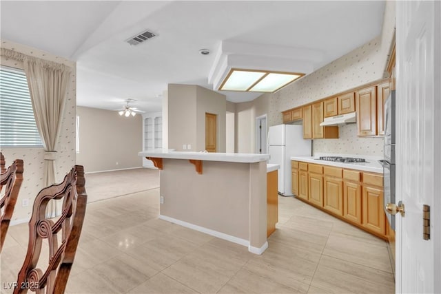 kitchen featuring a center island, white refrigerator, stainless steel gas cooktop, a kitchen bar, and light brown cabinets