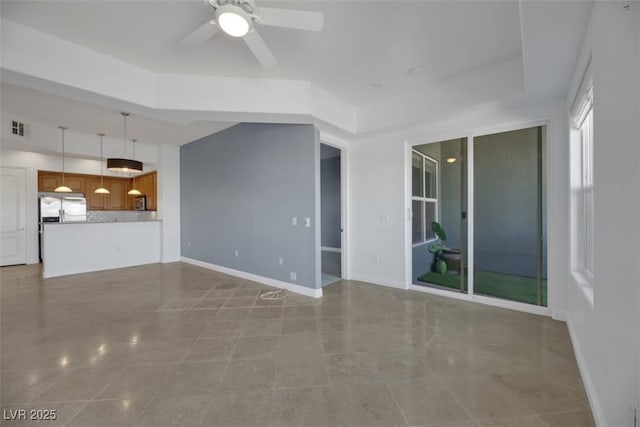 unfurnished living room with ceiling fan and a tray ceiling