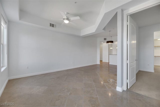 empty room with ceiling fan and a tray ceiling