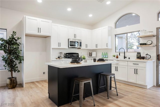 kitchen featuring sink, a kitchen breakfast bar, a center island, white cabinets, and light wood-type flooring