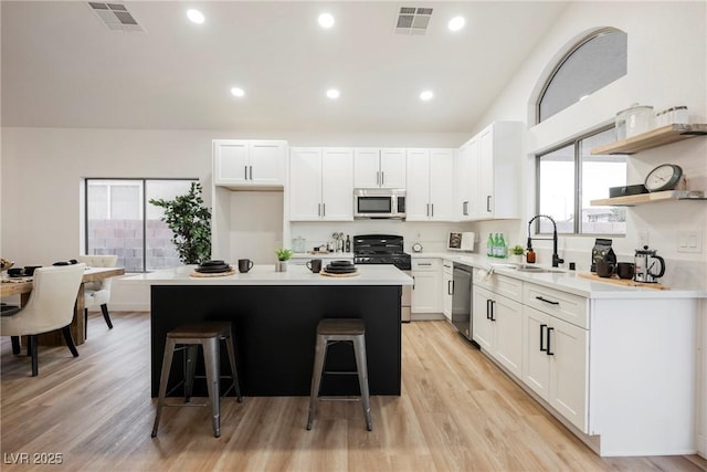 kitchen with appliances with stainless steel finishes, white cabinetry, sink, a breakfast bar area, and a center island