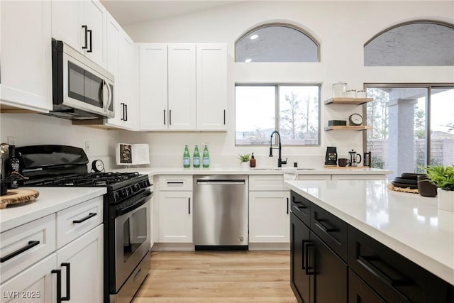 kitchen featuring sink, white cabinetry, stainless steel appliances, a healthy amount of sunlight, and vaulted ceiling