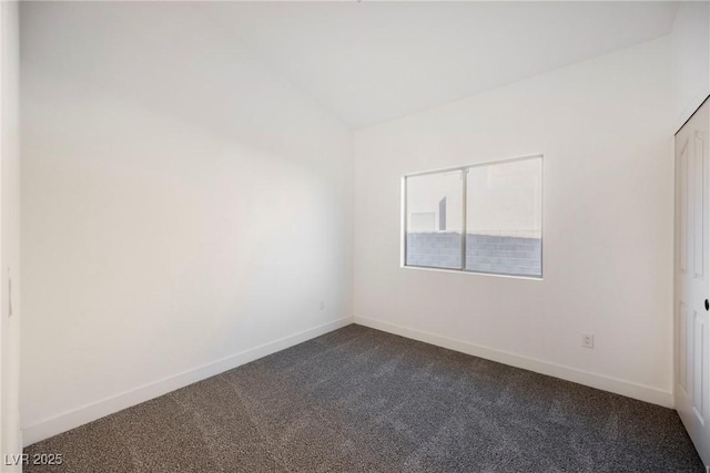 spare room featuring lofted ceiling and dark colored carpet