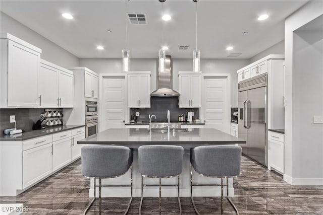 kitchen featuring pendant lighting, wall chimney range hood, white cabinets, and stainless steel built in fridge