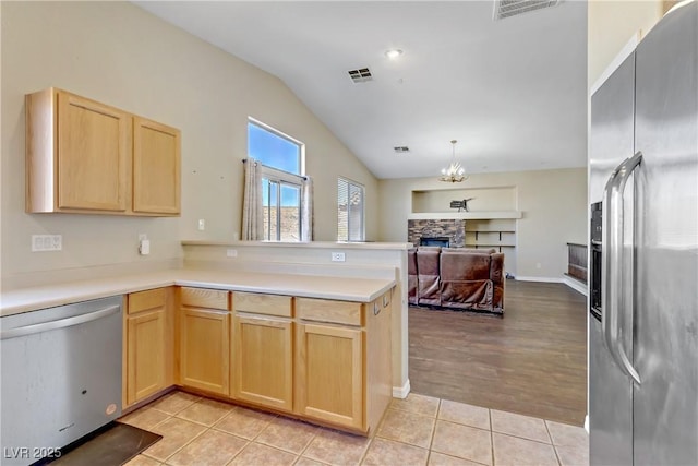 kitchen featuring light brown cabinetry, light tile patterned floors, appliances with stainless steel finishes, kitchen peninsula, and a fireplace