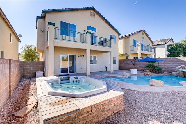 rear view of house featuring a swimming pool with hot tub and a balcony