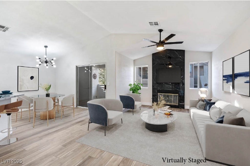 living room with lofted ceiling, a high end fireplace, light hardwood / wood-style flooring, and ceiling fan with notable chandelier