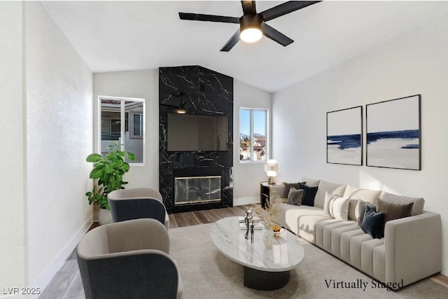 living room featuring ceiling fan, a high end fireplace, vaulted ceiling, and wood-type flooring