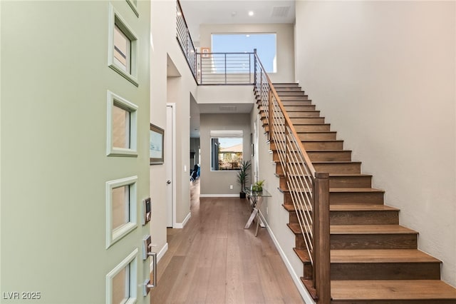 staircase featuring a healthy amount of sunlight, hardwood / wood-style floors, and a towering ceiling