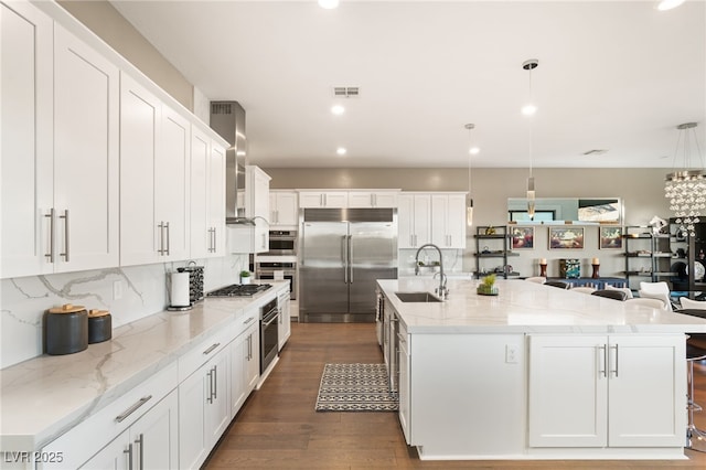 kitchen with pendant lighting, a large island, wall chimney range hood, and appliances with stainless steel finishes