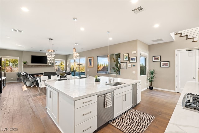 kitchen featuring white cabinetry, light stone countertops, stainless steel dishwasher, and an island with sink