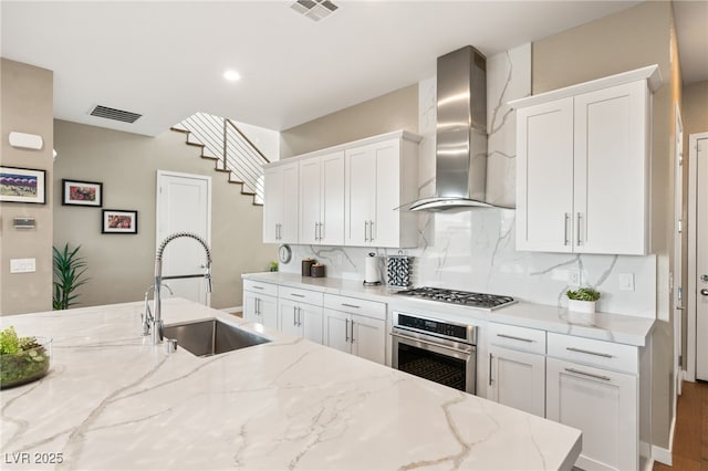 kitchen with appliances with stainless steel finishes, sink, wall chimney range hood, and light stone counters