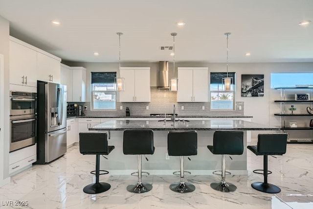 kitchen featuring stainless steel appliances, a center island with sink, white cabinets, and wall chimney exhaust hood