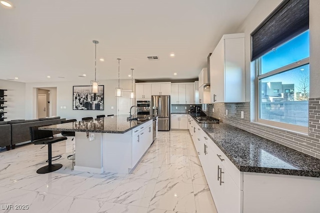 kitchen with sink, white cabinetry, hanging light fixtures, stainless steel appliances, and a spacious island