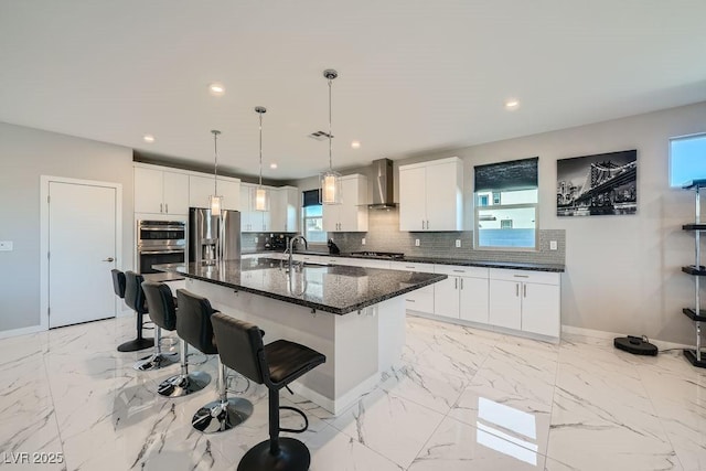 kitchen with wall chimney range hood, sink, white cabinets, and a center island with sink