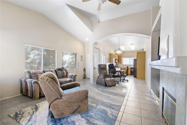 tiled living room with a tile fireplace, plenty of natural light, high vaulted ceiling, and ceiling fan