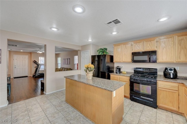 kitchen featuring a center island, light brown cabinetry, light stone counters, and black appliances