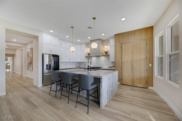 kitchen with pendant lighting, stainless steel fridge, a breakfast bar area, white cabinetry, and an island with sink