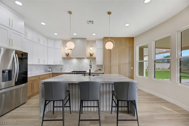 kitchen featuring pendant lighting, light stone countertops, an island with sink, white cabinets, and stainless steel fridge with ice dispenser