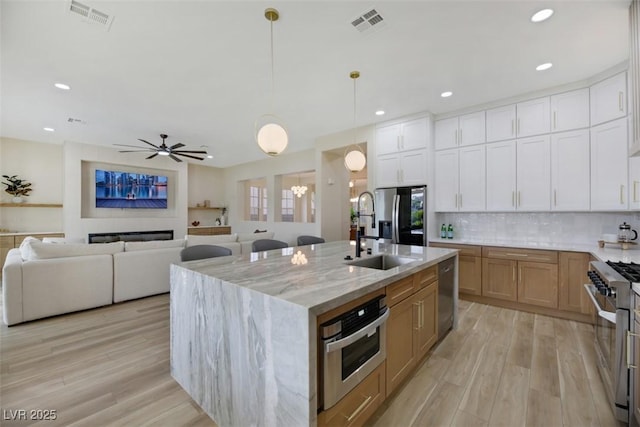 kitchen featuring white cabinetry, stainless steel appliances, light stone countertops, and a kitchen island with sink